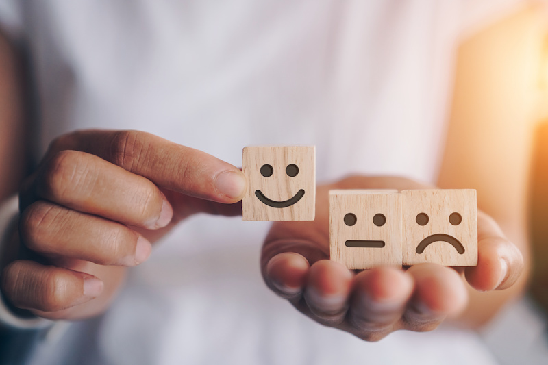 A person putting a "happy" face wood block next to a meh and unhappy one